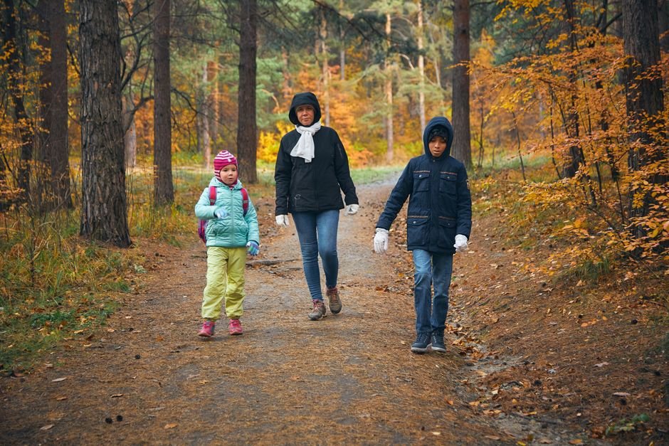 Une mère et deux enfants marchent ensemble sur un sentier en forêt